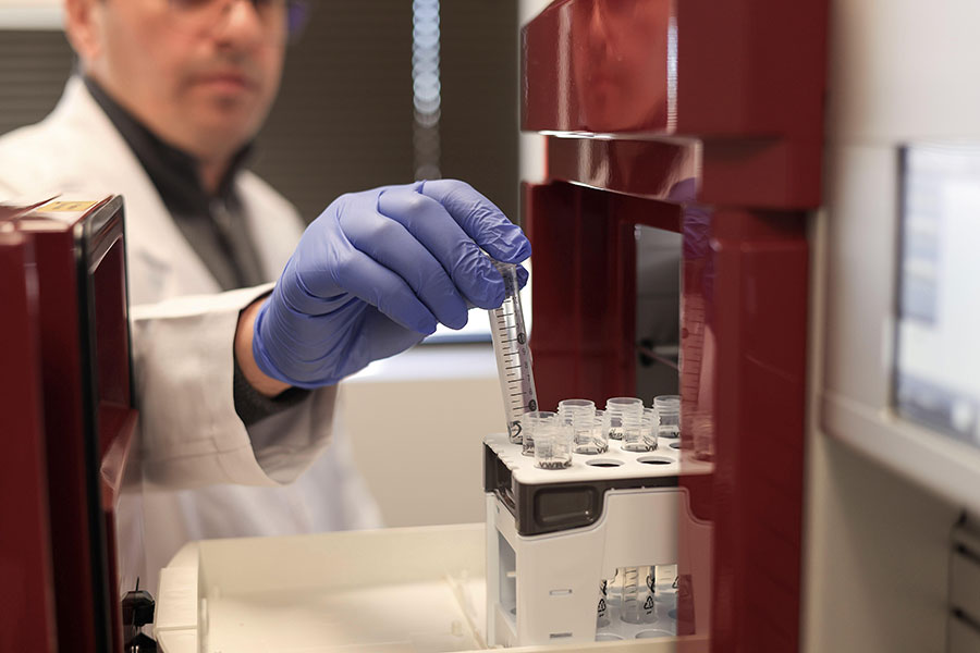 An individual with a blue glove holding a small vial.