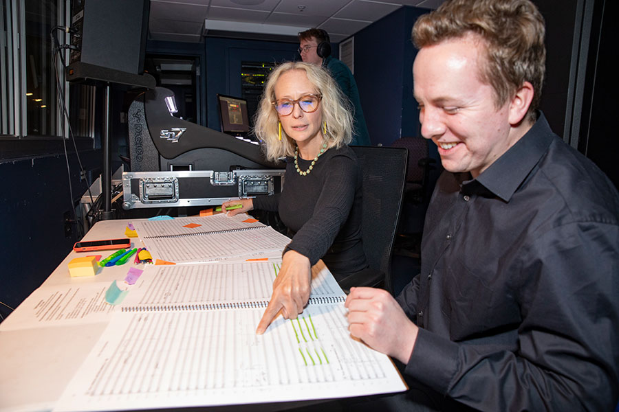 A woman points at a music sheet on a table next to a man smiling.