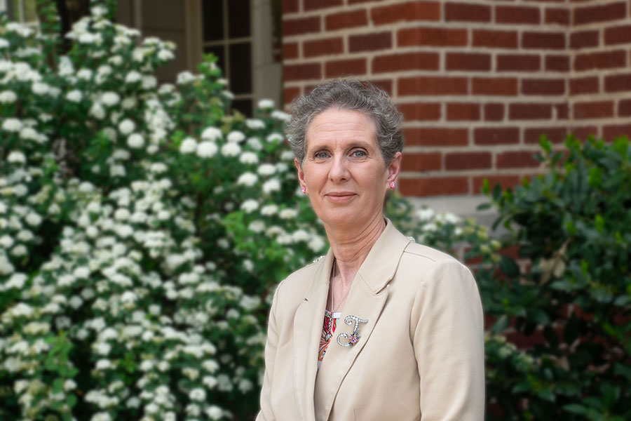 June Abbas stands outside in front of brick building and bushes.