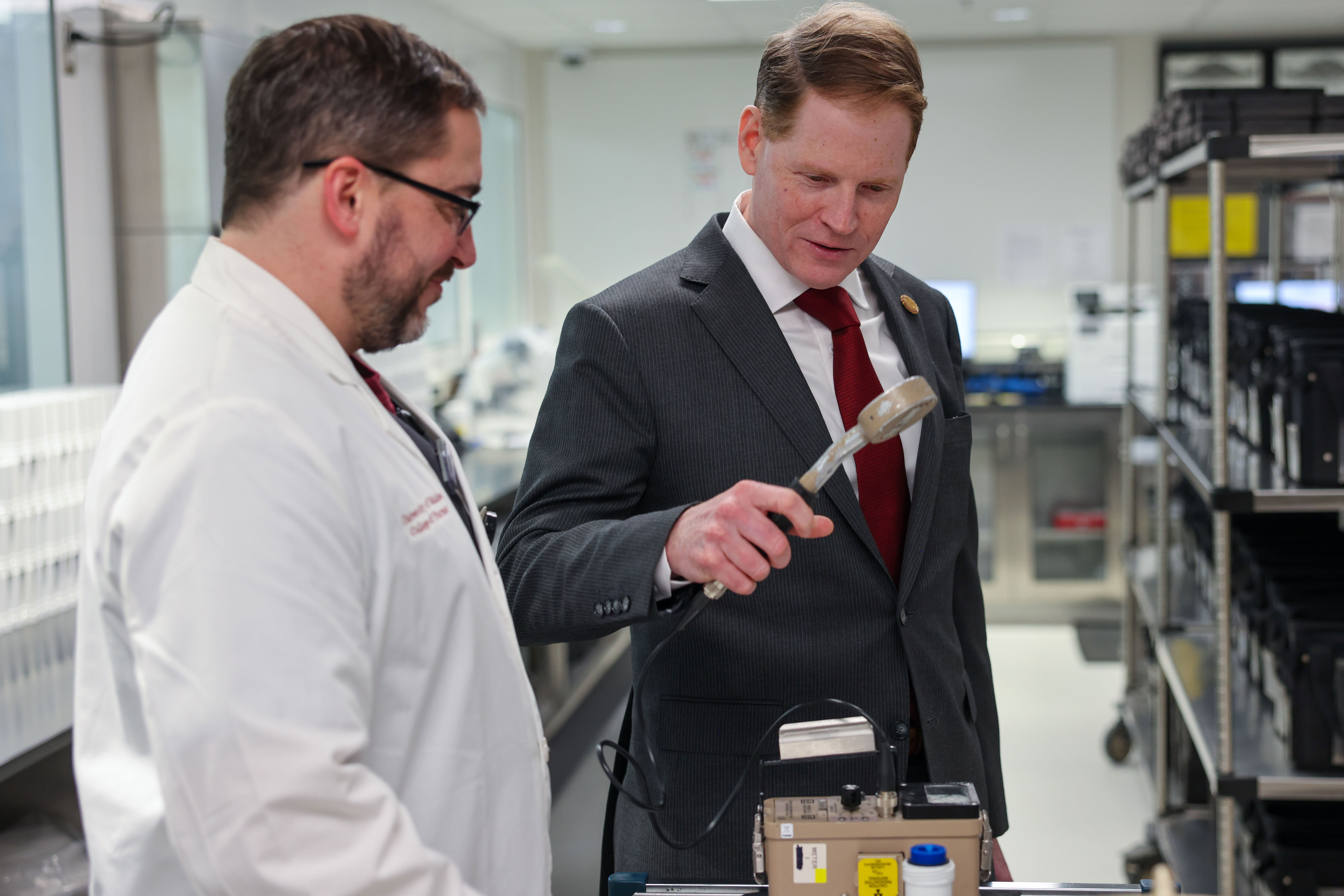 A doctor in a white coat and a man in a grey suit examine medical technology.