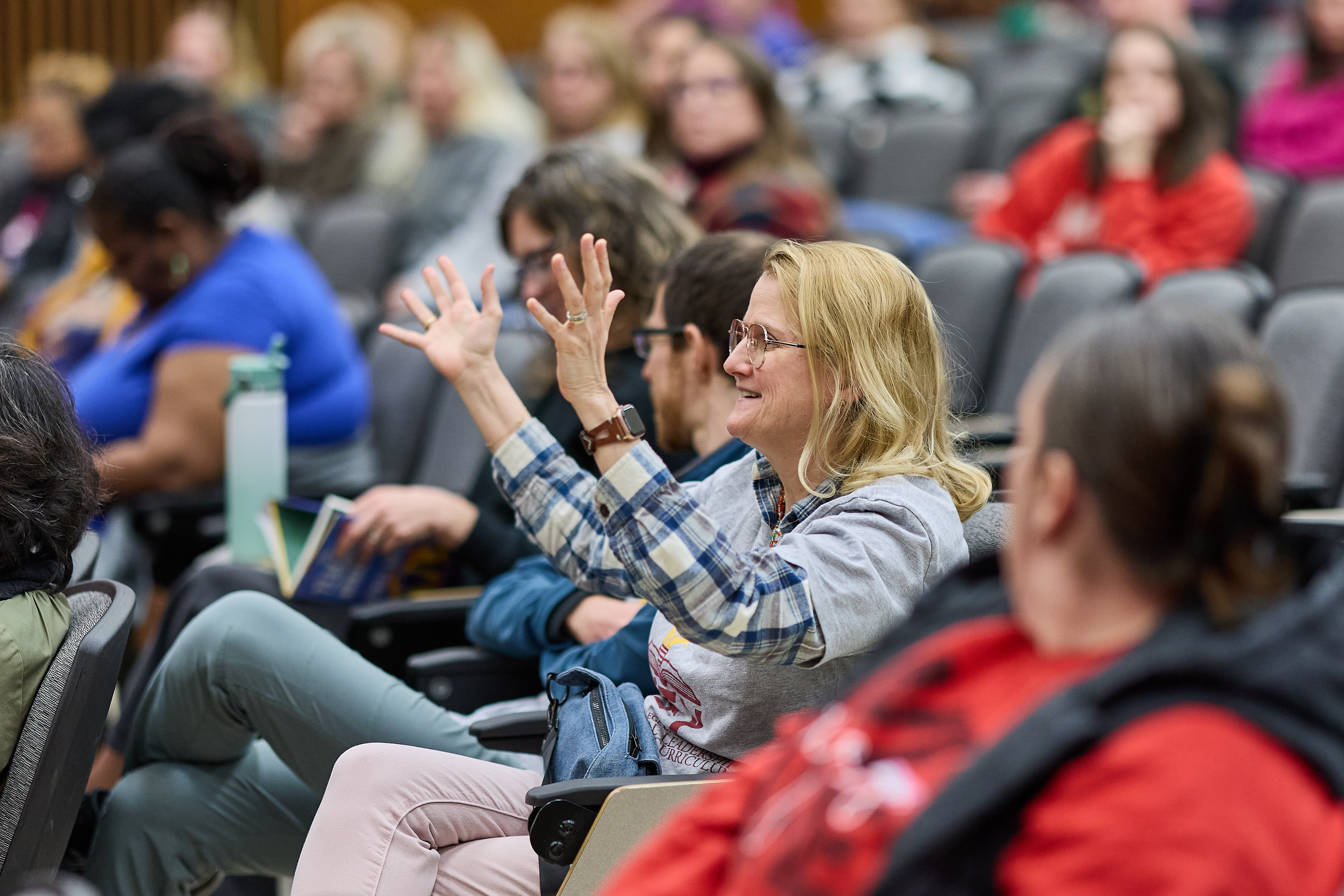 A woman sitting in an auditorium lifting her hands and speaking. 