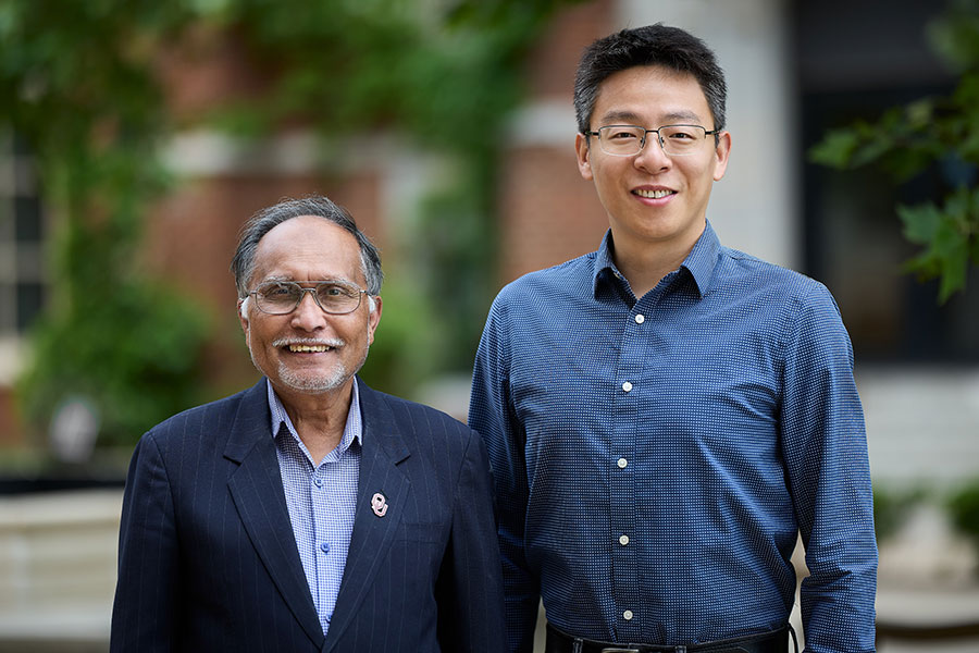 A man in a suit and a man in a buttoned dress shirt stand outside.