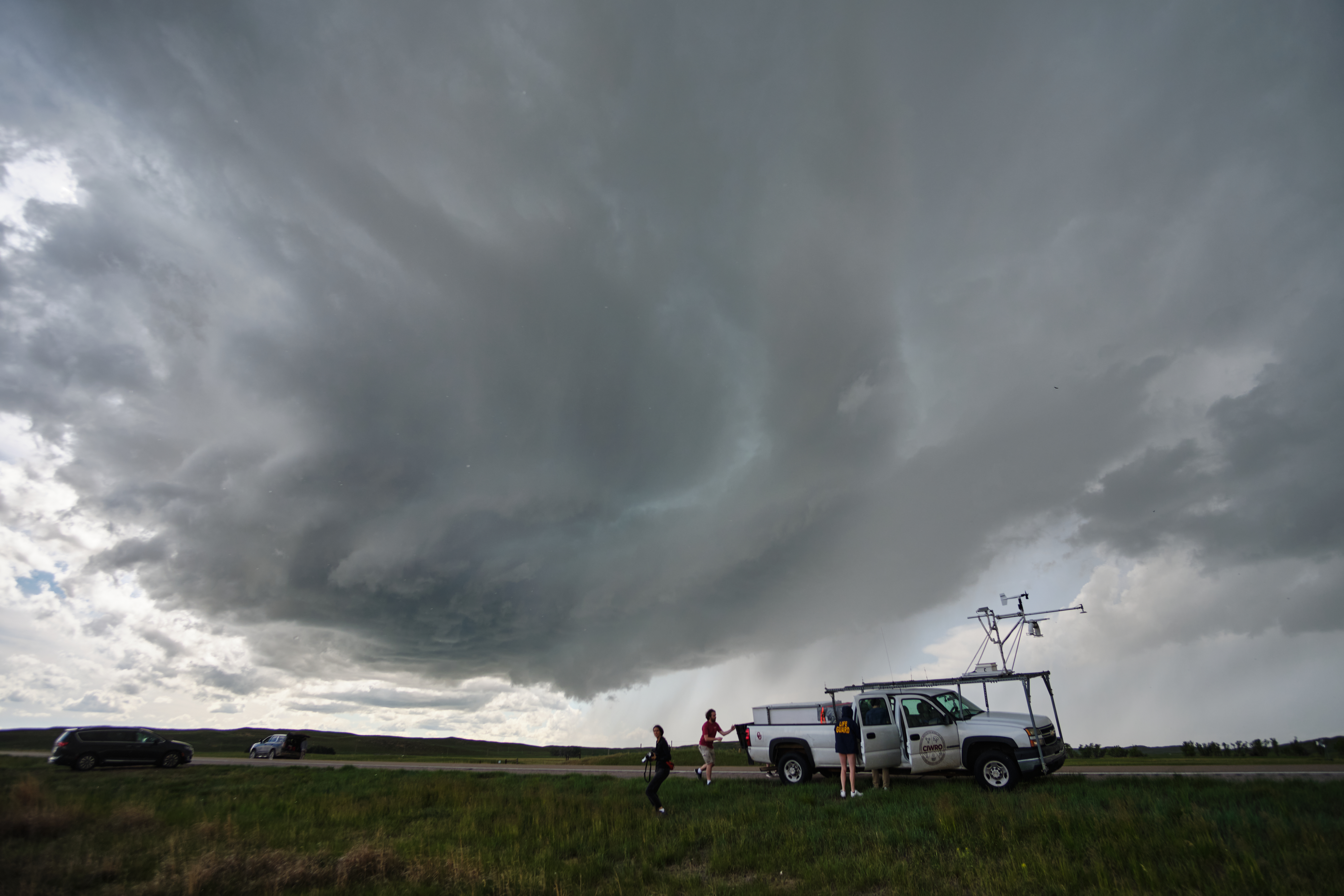 A truck on the side of the road with a vast cloud in the background.