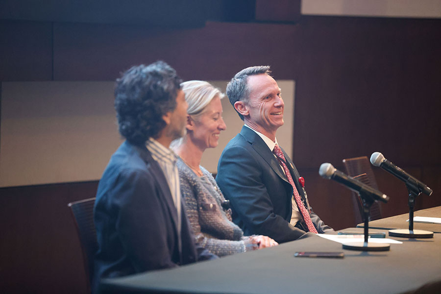 Three people sit at a long table in front of microphones.
