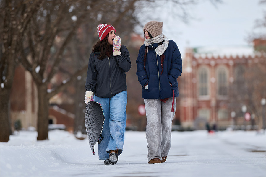 Two warmly dressed students explore the snow on campus.