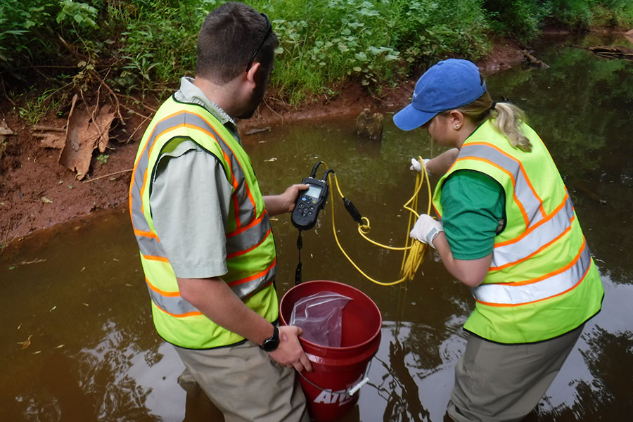 Two people with equipment taking a water sample from a river.
