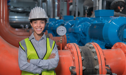 A person in a hardhat standing in front of pipes.