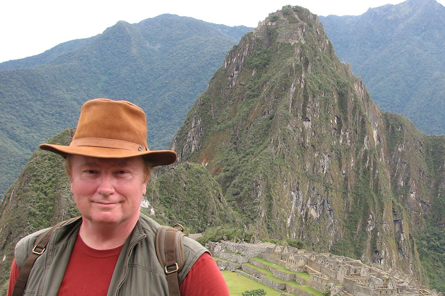 Steve Gullberg wearing a hat and hiking gear, with mountains in the background.