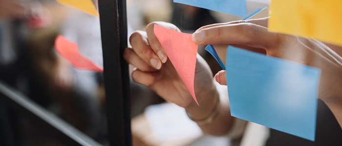 Close up of hands placing different coloured sticky notes on a glass board
