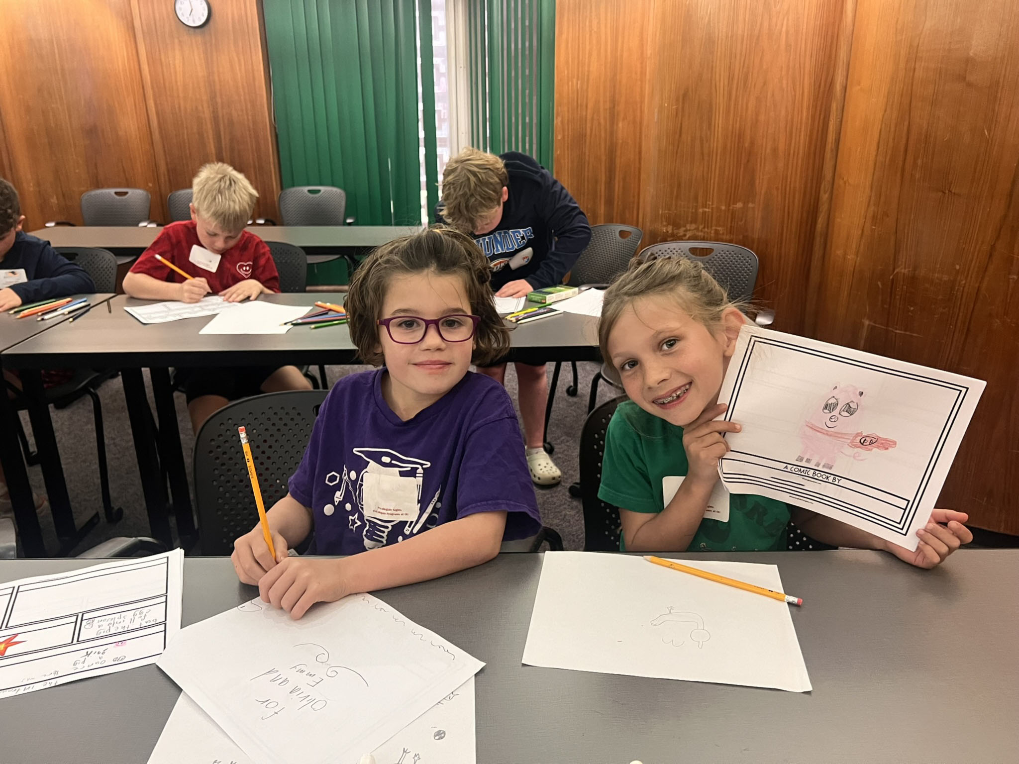 Two kids sitting at a table with project work. 