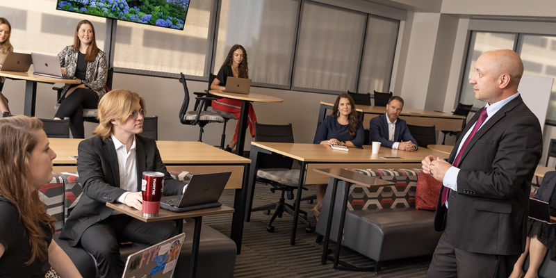 A professor stands in front of a room of students while giving a lecture.