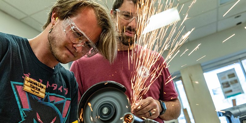 two men wearing safety goggles work together on equipment in the iHub Fab Lab. 