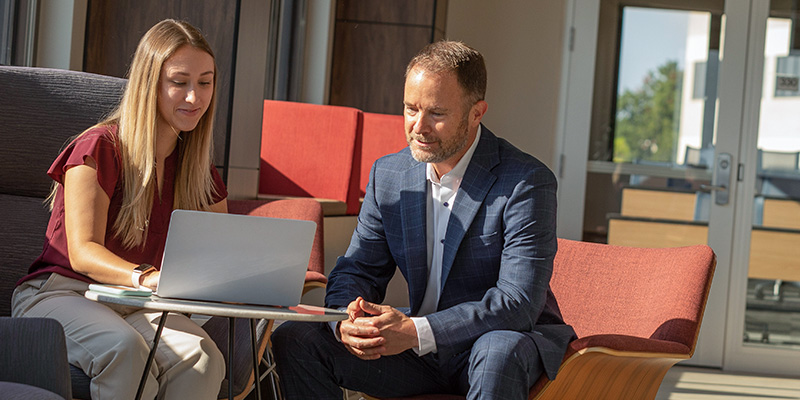 two professionals sit together in the graduate center while they collaborate on a laptop
