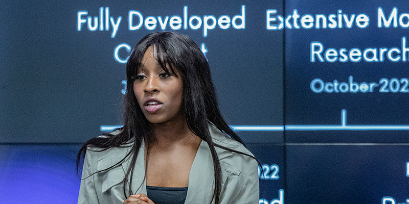 A speaker stands in front of a presentation srcreen while delivering her message .