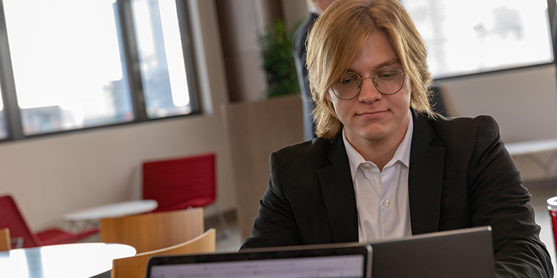 A young man sits at a table working on a laptop in the downtown OKC graduate center