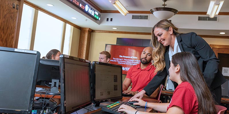 A professor helps a student in the Adams Hall computer lab, while several other students work on computers