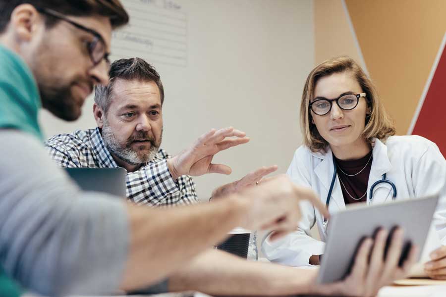 A doctor and two other people sitting around a table discussing work. 