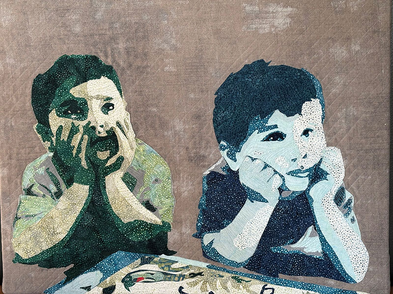 Two children quilted in green and blue with their hands propping up their faces in deep thought.