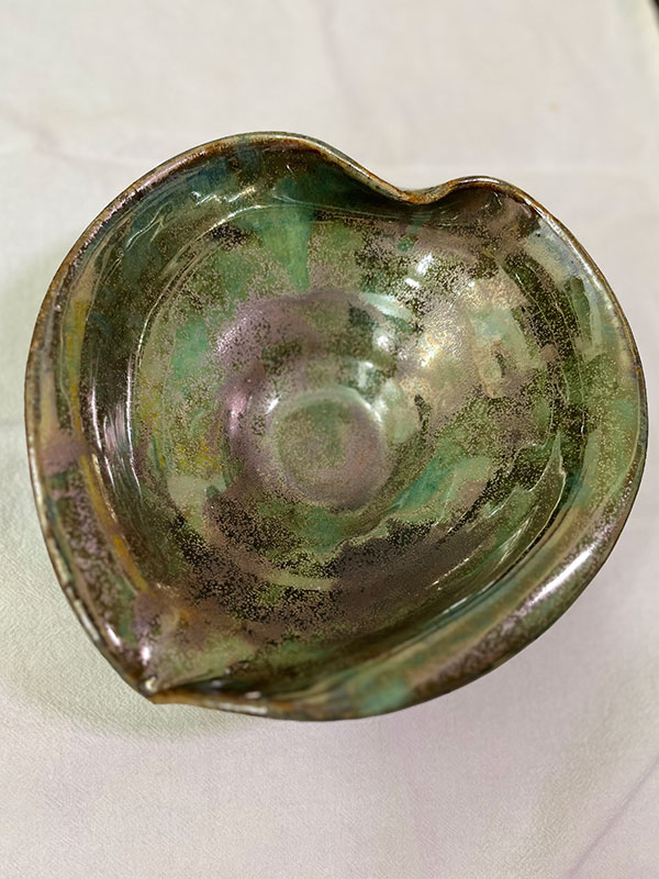 A ceramic form of a leaf shaped bowl, glazed with green and brown.