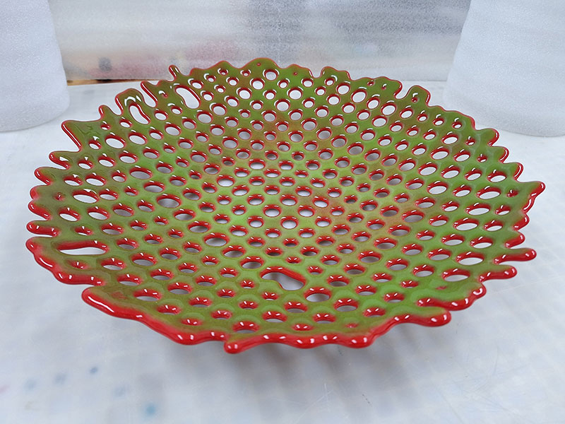 Fused green glass overlaying red glass, round form with irregular holes.