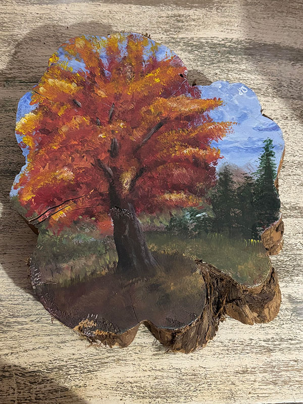 A painting of a fall tree painting on a wooden stump.