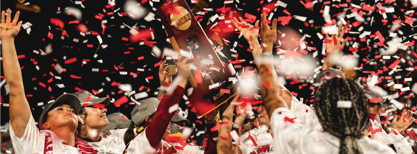 Several students are cheering at a football game, a large crowd can be seen in the background